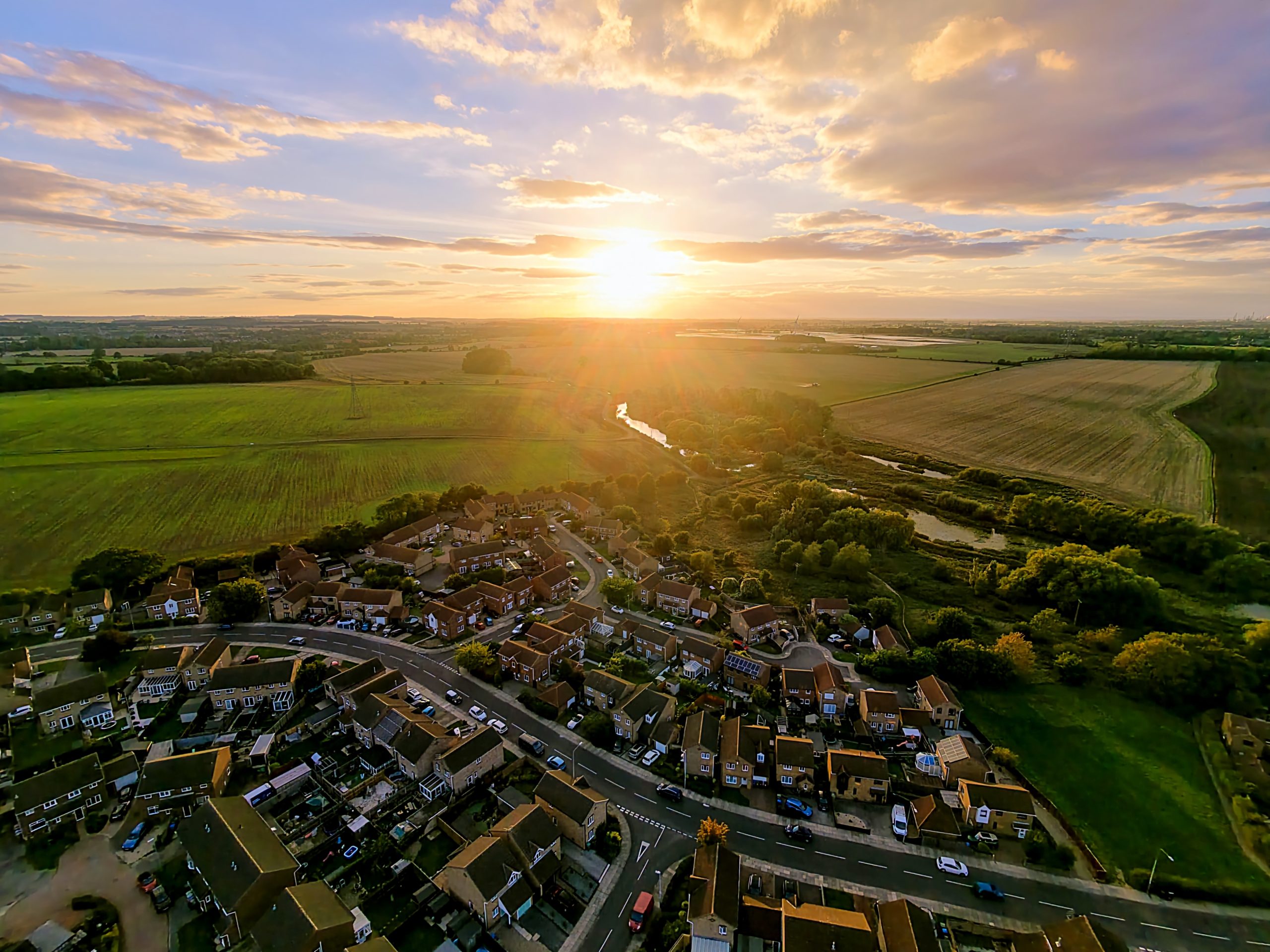 Aerial sunset over Lincolnshire fields, river and homes