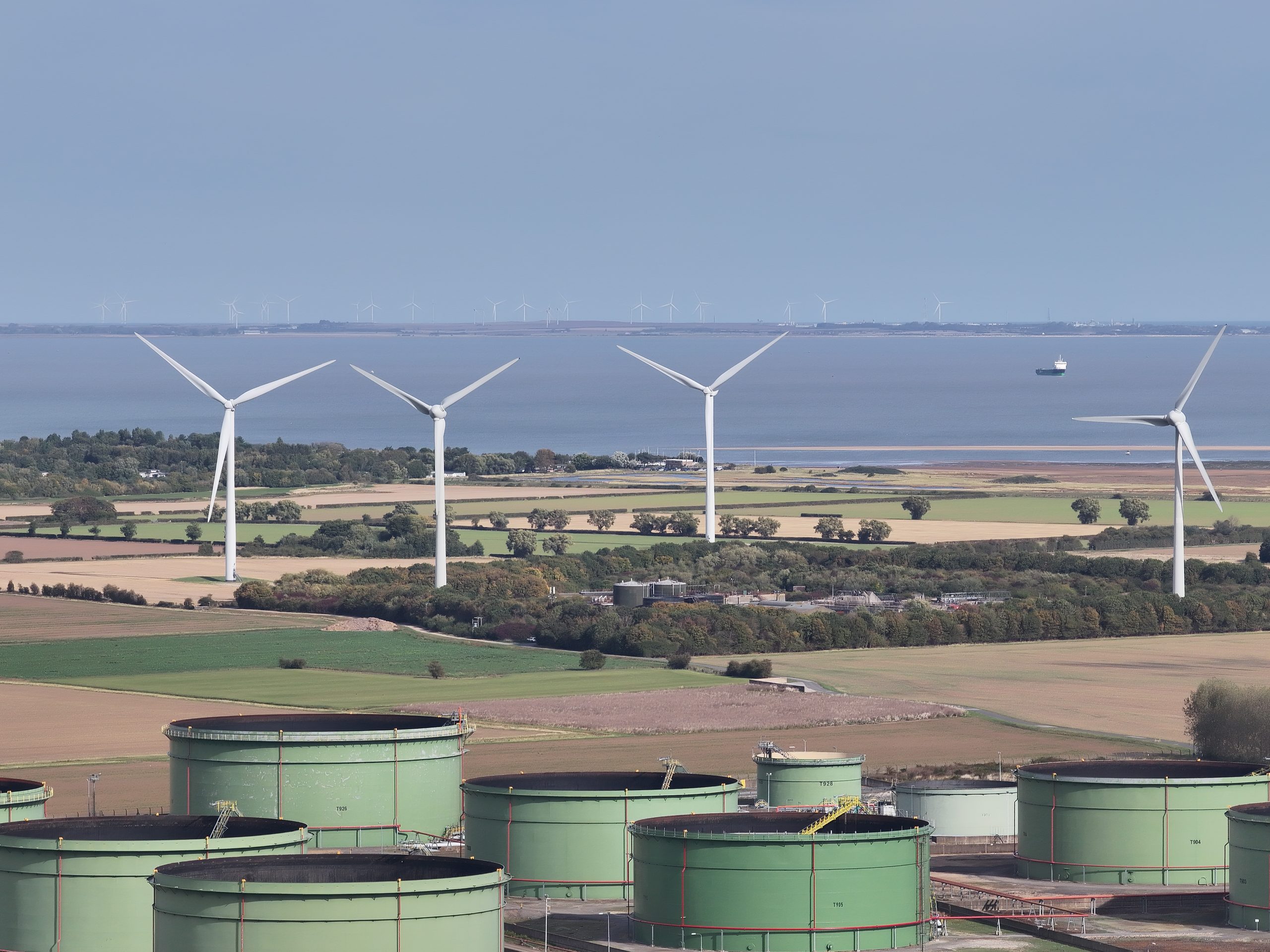 Aerial photograph of wind turbines, industrial storage tanks and the river beyond.