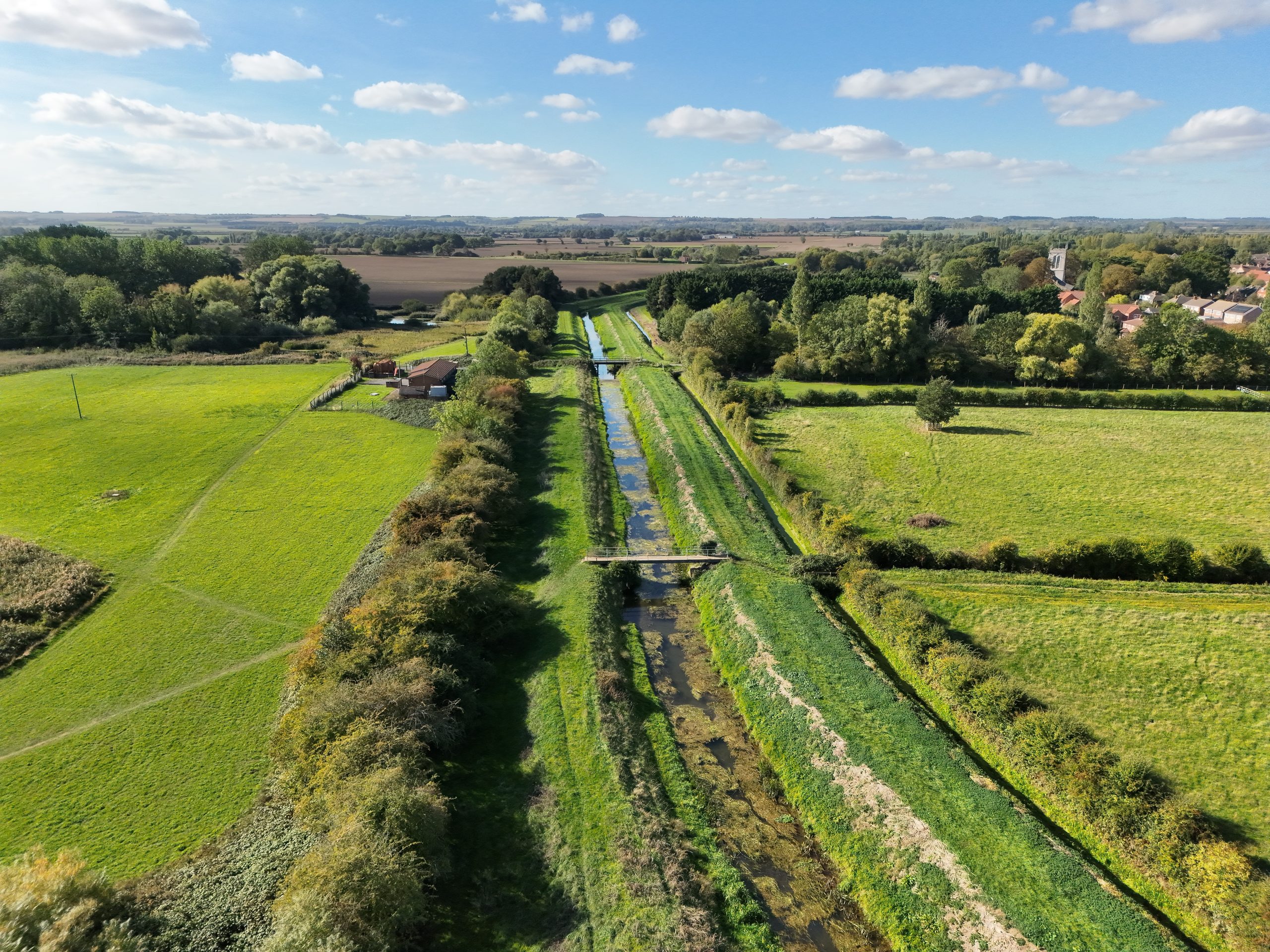 Aerial view along a Lincolnshire waterway through green fields, trees and villages